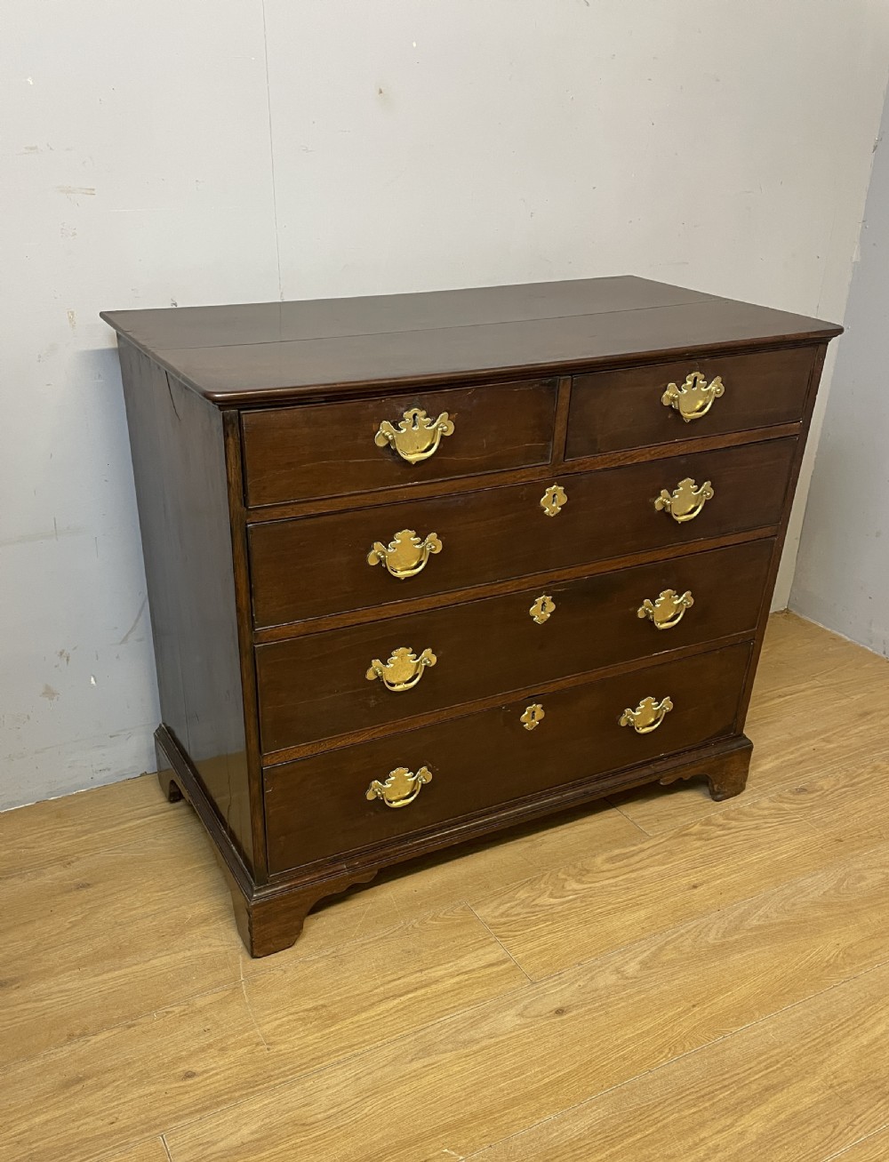 A late 18th-century Georgian solid mahogany four-height chest of drawers with two short over three long drawers, brass handles, and bracket feet.