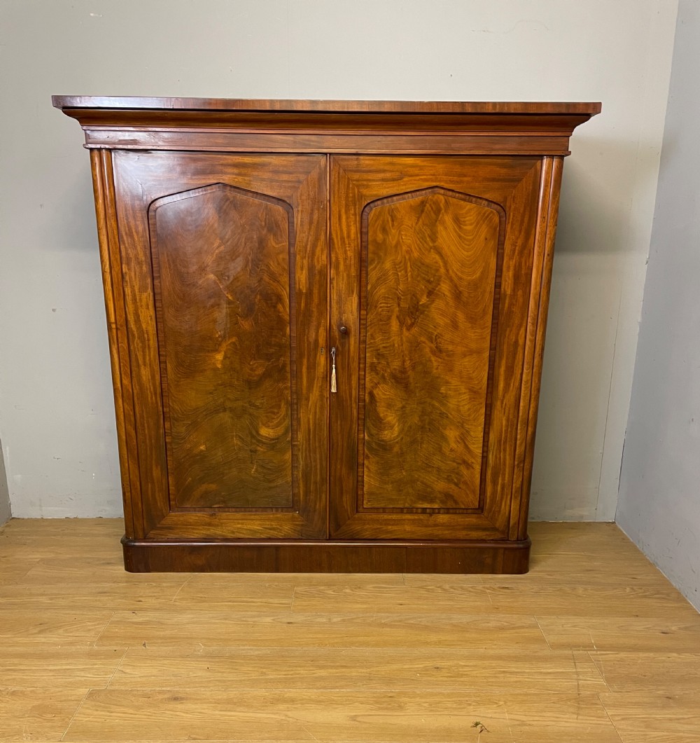 A nineteenth-century flame mahogany two-door library cupboard with arched door panels and a plinth base. View XVII
