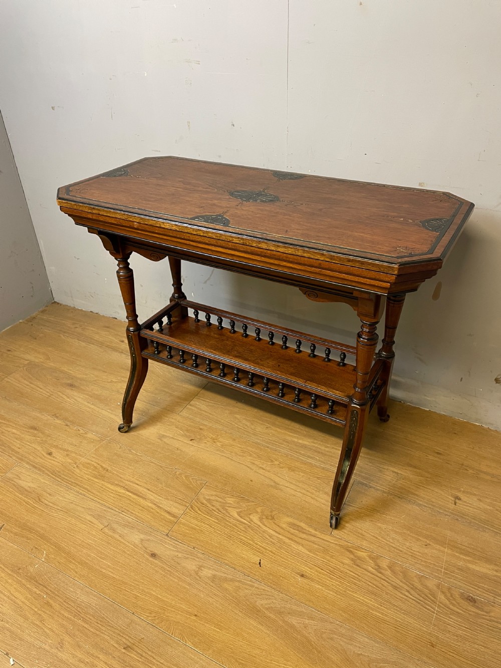 A late 19th-century Aesthetic Movement oak card table with incised top decorations, turned legs, and a lower spindle gallery shelf.