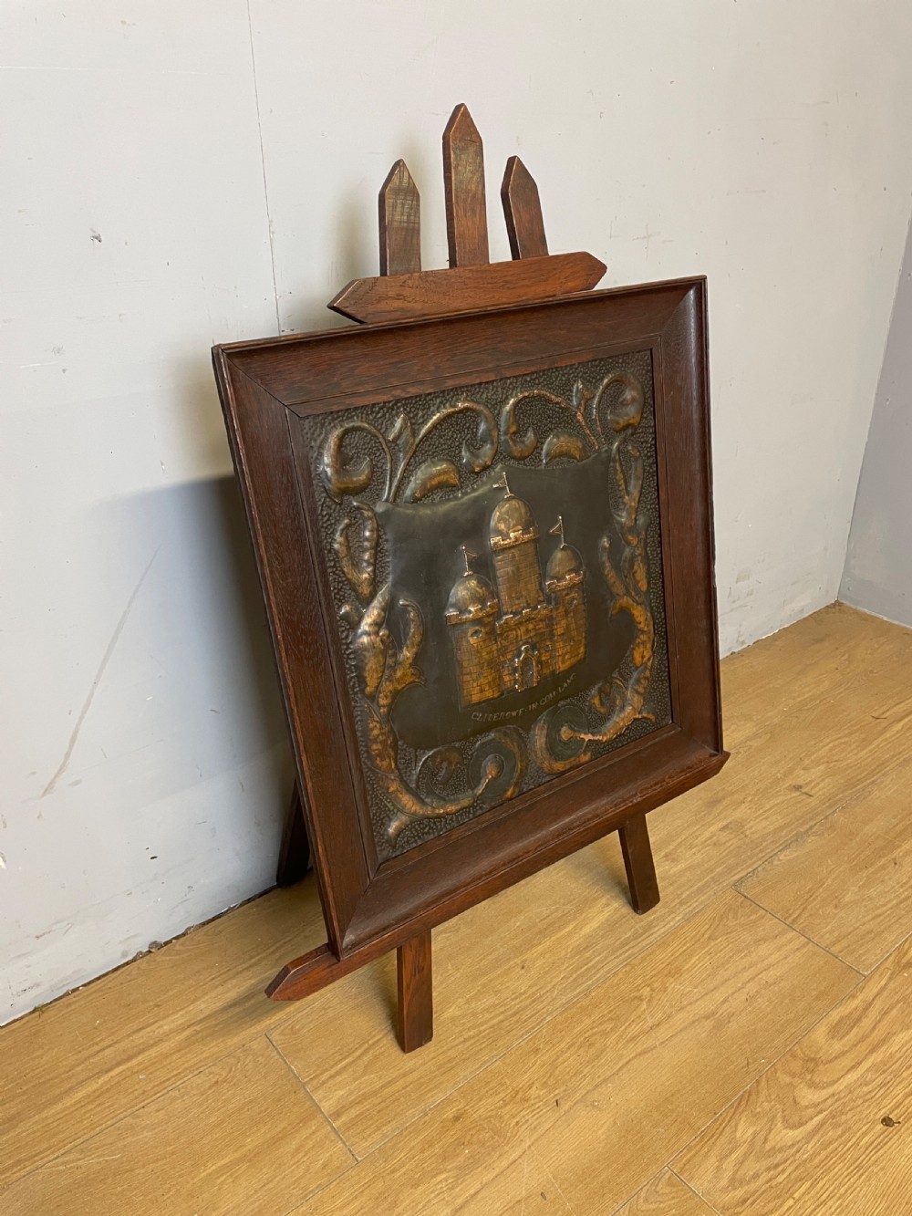 An Arts and Crafts dark oak framed firescreen featuring a central hand-hammered copper panel with an embossed castle motif and scrollwork. View III