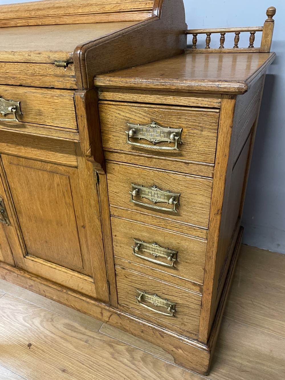 A nineteenth-century golden oak tambour desk featuring multiple side drawers with brass handles, central panelled cupboard doors, and a raised wooden gallery rail. View III