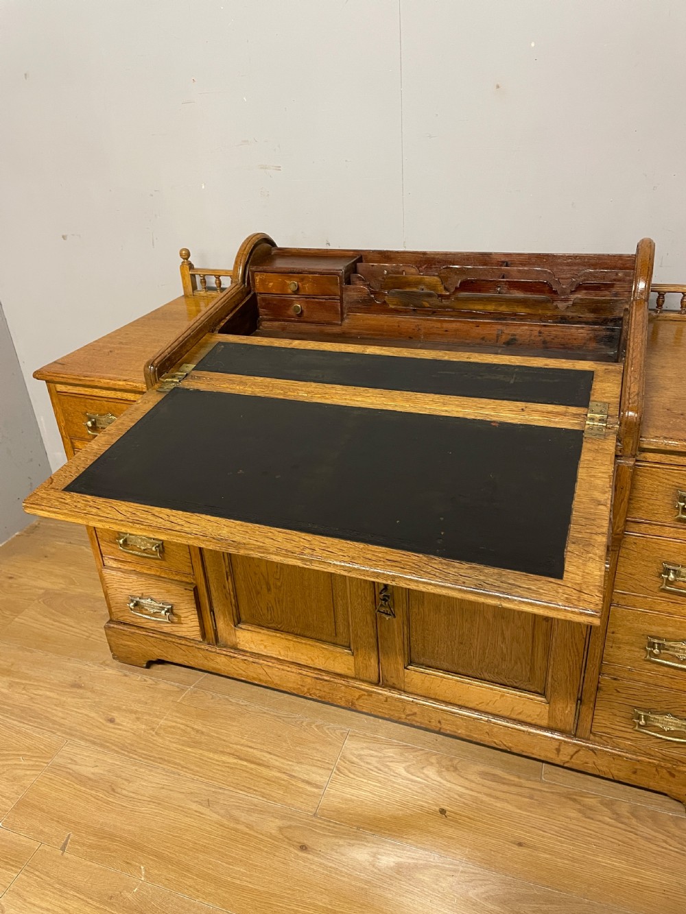 A nineteenth-century golden oak tambour desk featuring multiple side drawers with brass handles, central panelled cupboard doors, and a raised wooden gallery rail. View V