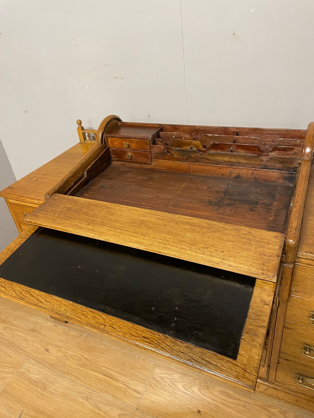 A nineteenth-century golden oak tambour desk featuring multiple side drawers with brass handles, central panelled cupboard doors, and a raised wooden gallery rail. View VI
