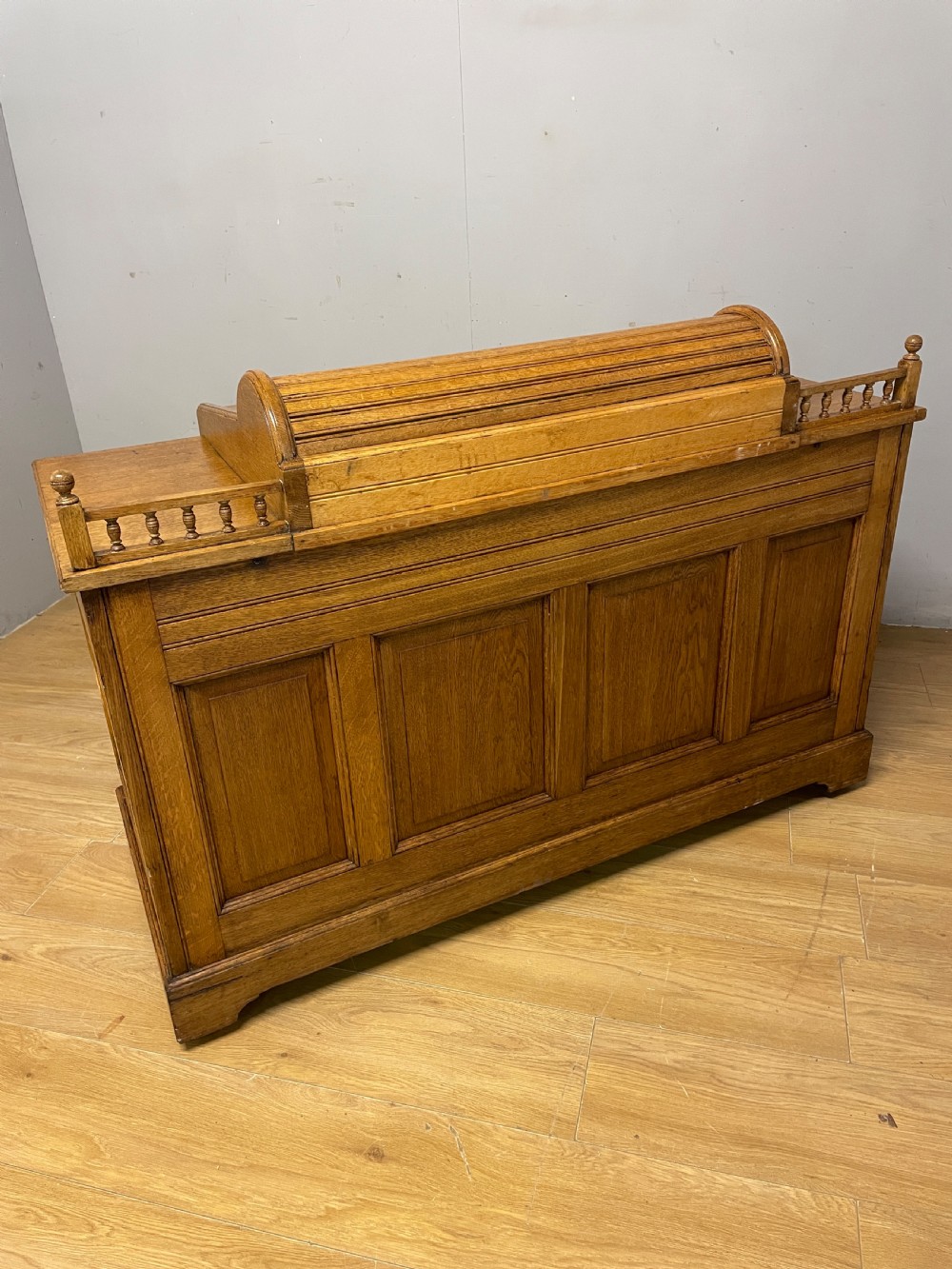 A nineteenth-century golden oak tambour desk featuring multiple side drawers with brass handles, central panelled cupboard doors, and a raised wooden gallery rail. View XI