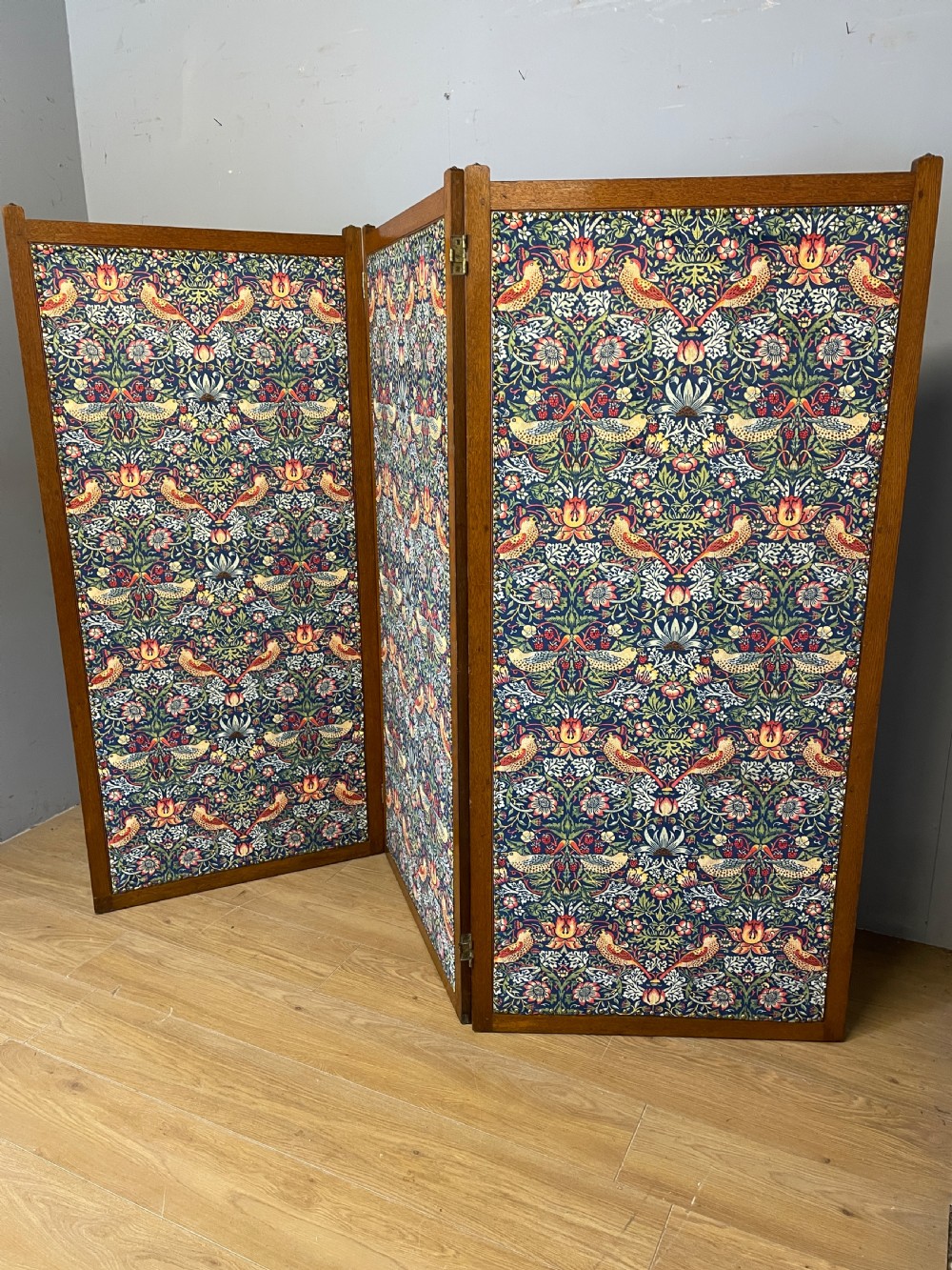 A three-panel wooden folding room screen framed in medium oak and upholstered with William Morris Strawberry Thief pattern velvet fabric in blue, red, and yellow tones. View II