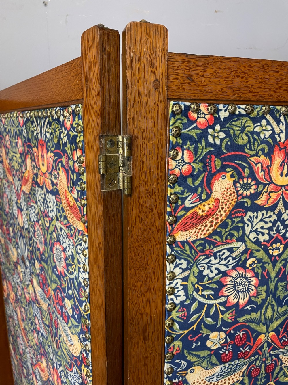 A three-panel wooden folding room screen framed in medium oak and upholstered with William Morris Strawberry Thief pattern velvet fabric in blue, red, and yellow tones. View III