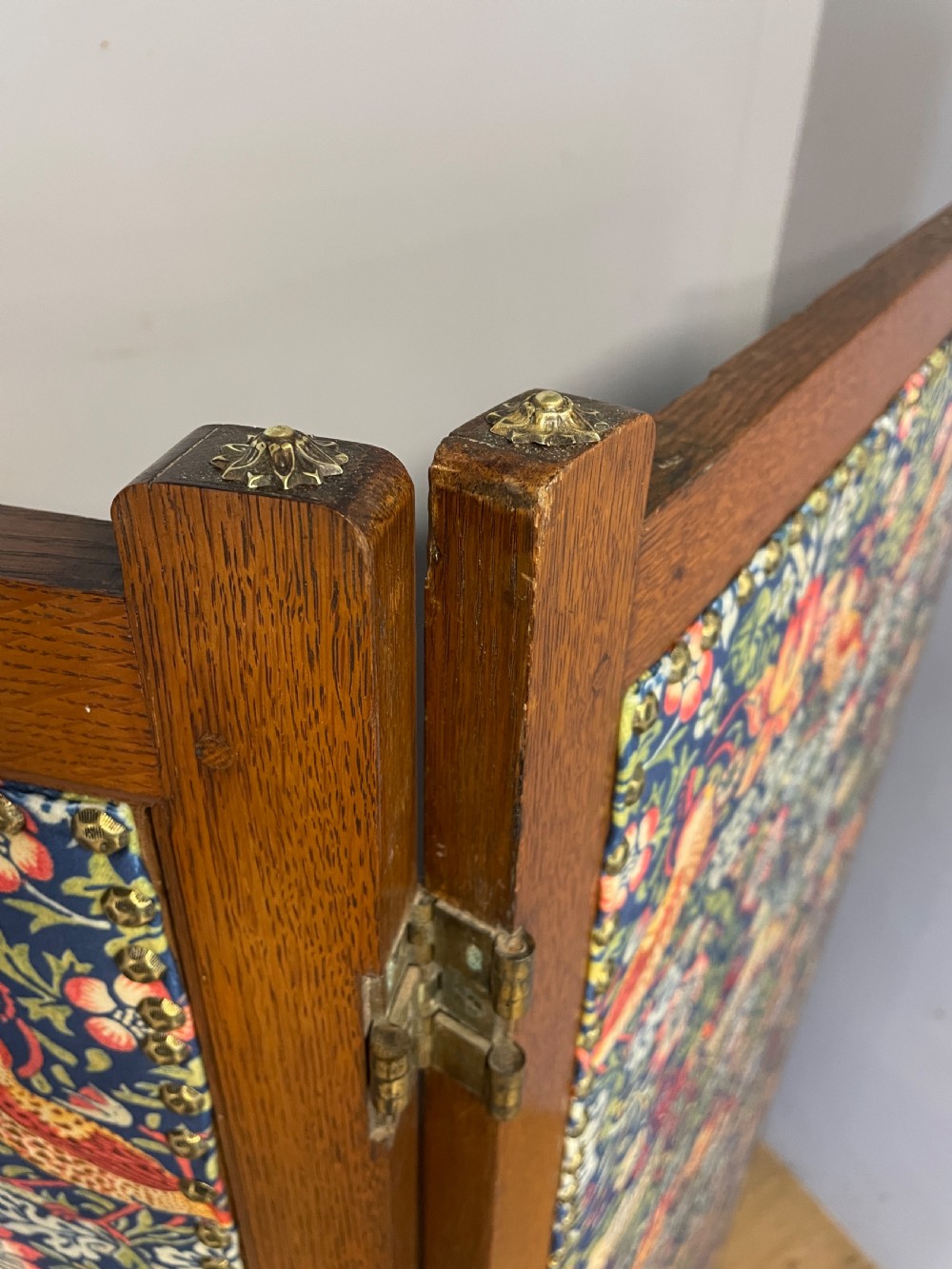A three-panel wooden folding room screen framed in medium oak and upholstered with William Morris Strawberry Thief pattern velvet fabric in blue, red, and yellow tones. View IV