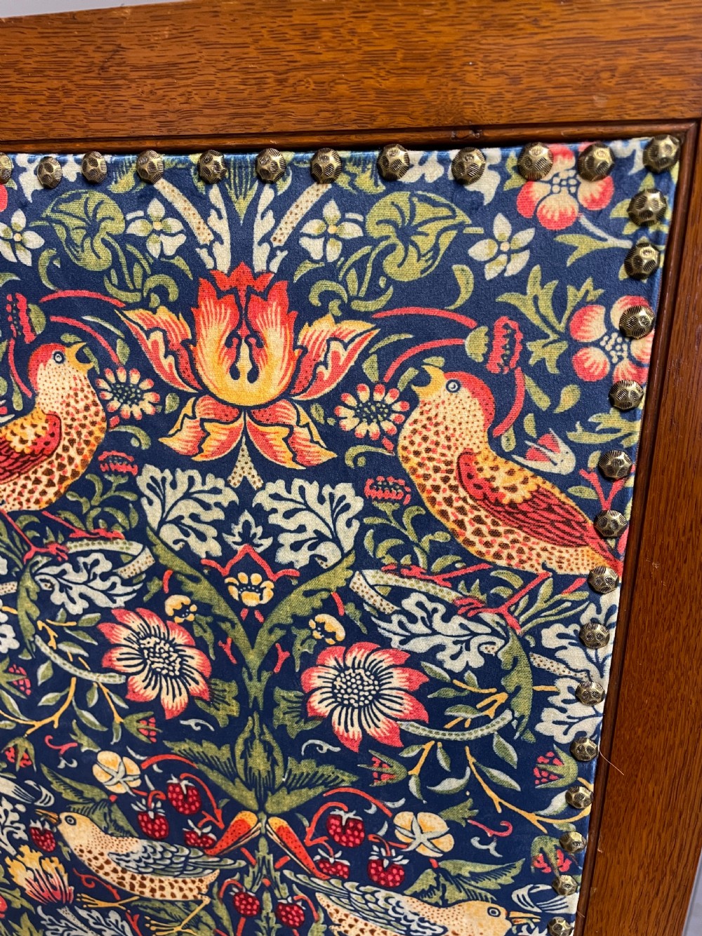 A three-panel wooden folding room screen framed in medium oak and upholstered with William Morris Strawberry Thief pattern velvet fabric in blue, red, and yellow tones. View VIII