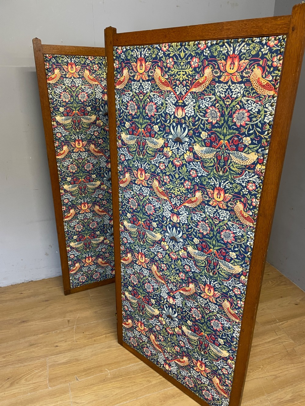 A three-panel wooden folding room screen framed in medium oak and upholstered with William Morris Strawberry Thief pattern velvet fabric in blue, red, and yellow tones. View X