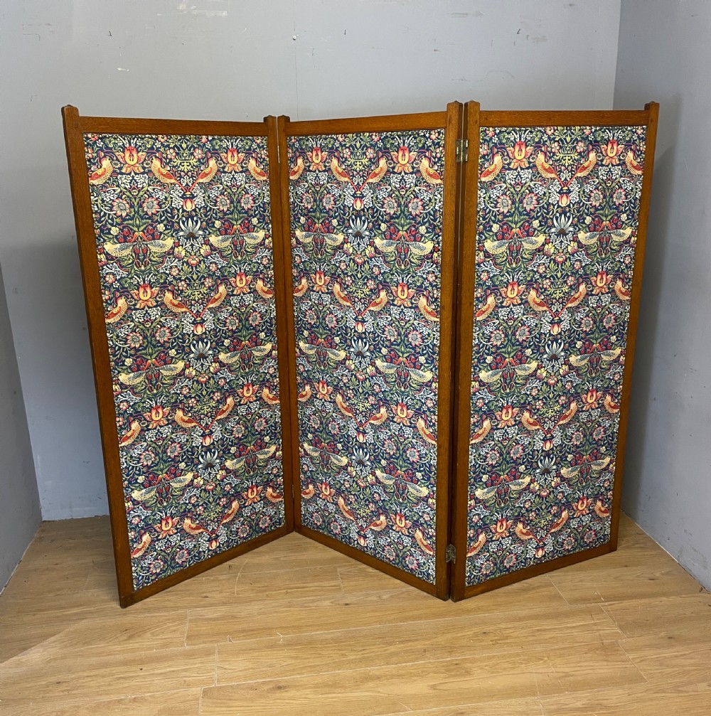 A three-panel wooden folding room screen framed in medium oak and upholstered with William Morris Strawberry Thief pattern velvet fabric in blue, red, and yellow tones. View XI