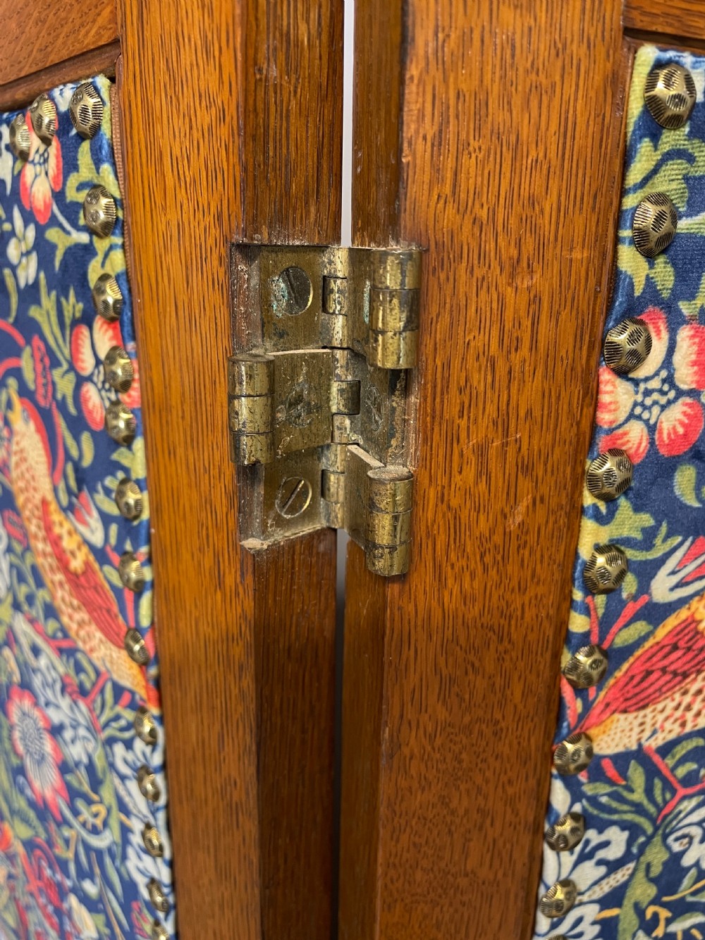 A three-panel wooden folding room screen framed in medium oak and upholstered with William Morris Strawberry Thief pattern velvet fabric in blue, red, and yellow tones. View XII