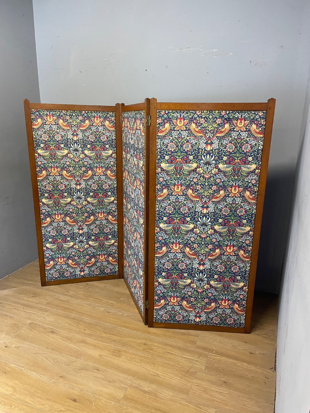 A three-panel wooden folding room screen framed in medium oak and upholstered with William Morris Strawberry Thief pattern velvet fabric in blue, red, and yellow tones. View XIII