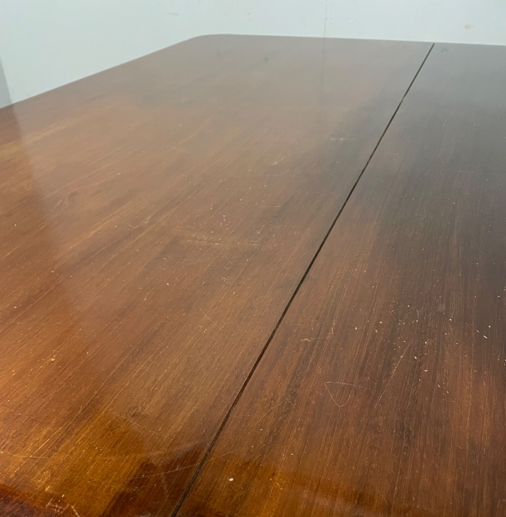 A William IV mahogany tilt-top dining table featuring a rectangular polished top with rounded corners supported by a central turned pedestal and four splayed legs with brass castors. View V
