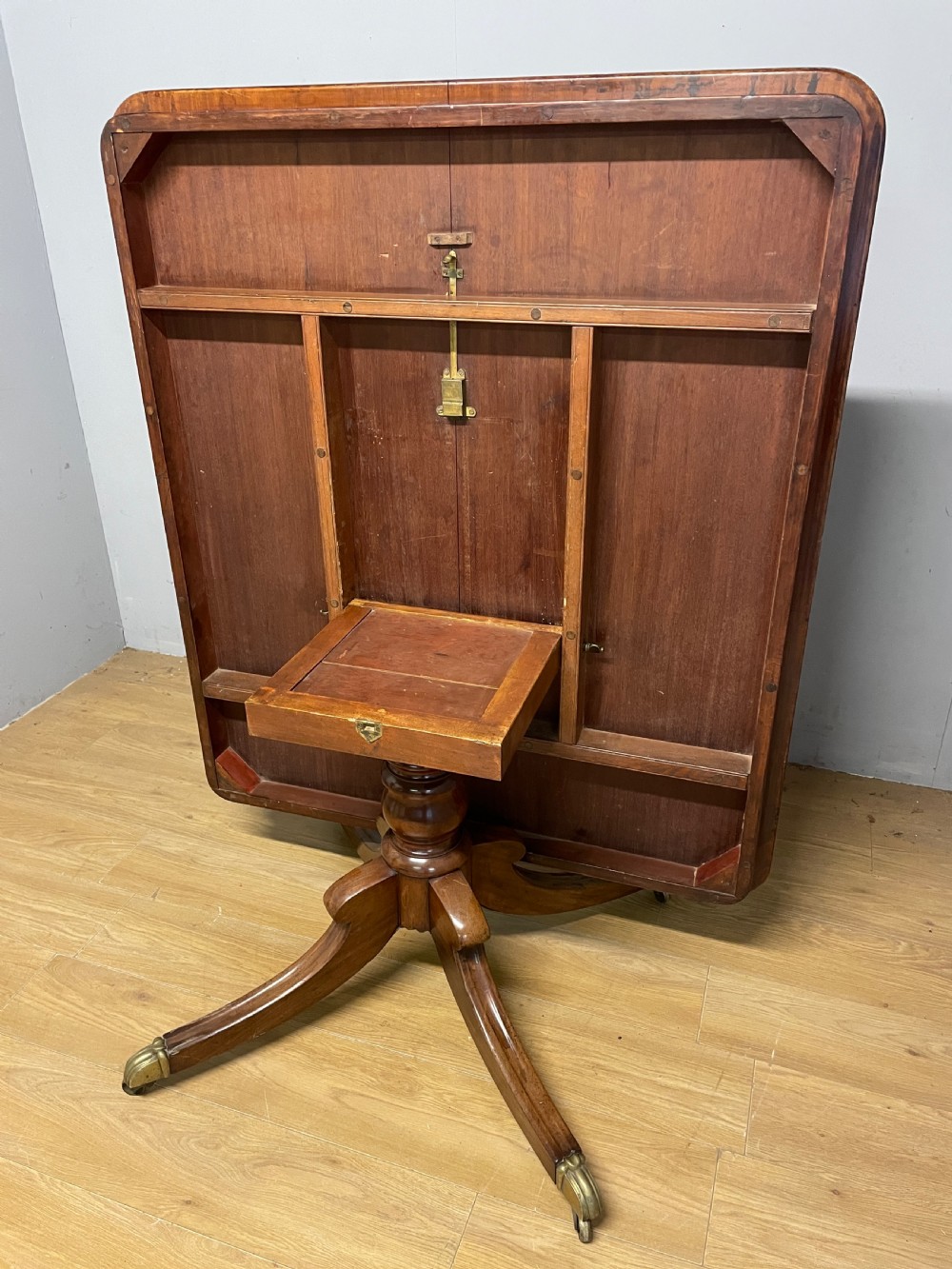 A William IV mahogany tilt-top dining table featuring a rectangular polished top with rounded corners supported by a central turned pedestal and four splayed legs with brass castors. View VI
