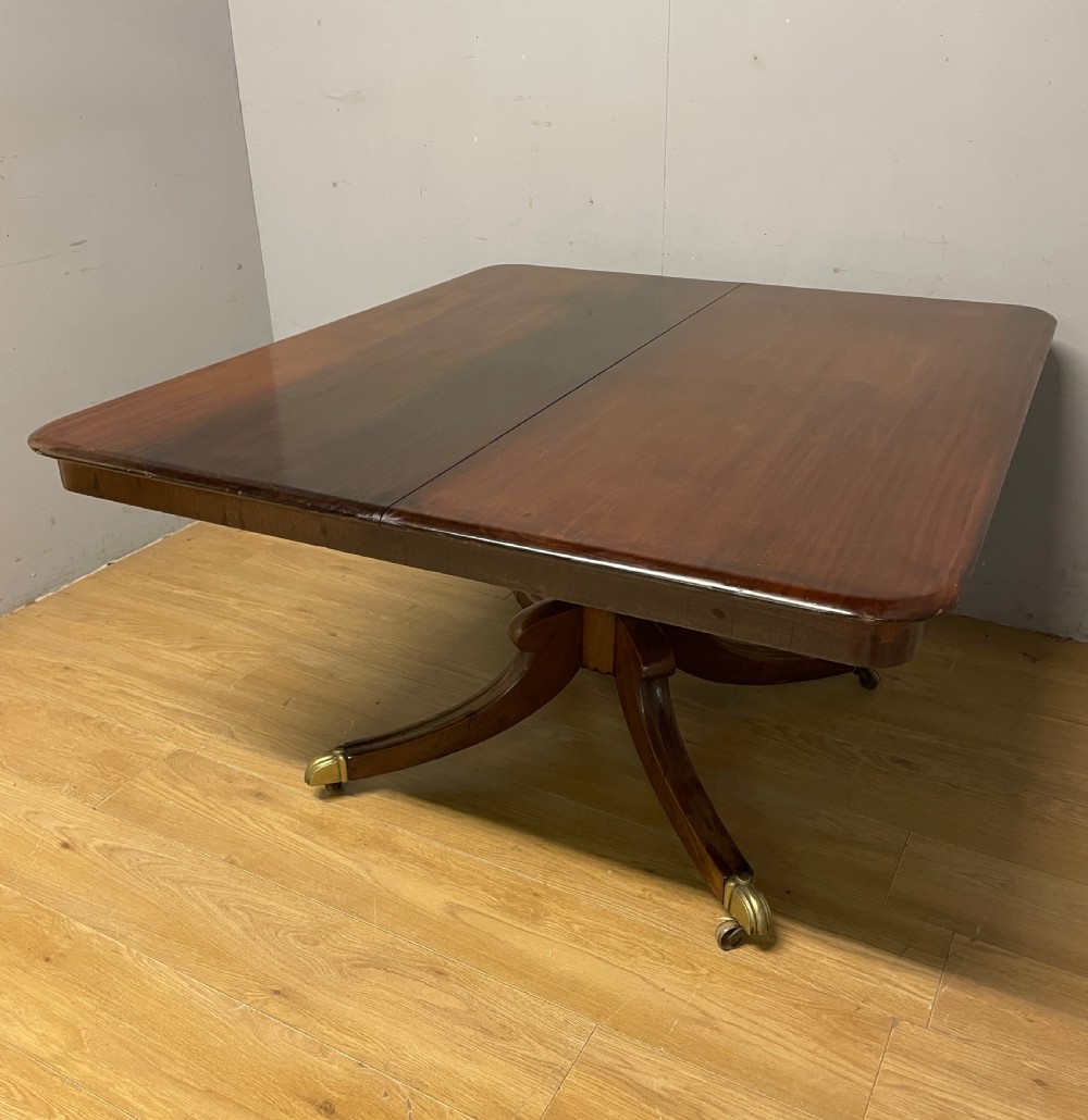 A William IV mahogany tilt-top dining table featuring a rectangular polished top with rounded corners supported by a central turned pedestal and four splayed legs with brass castors. View VIII