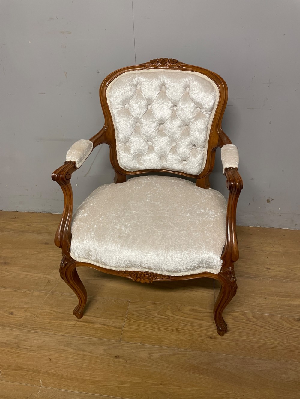 A Louis XV style solid walnut armchair featuring button-tufted cream velvet upholstery, carved cresting, and cabriole legs.
