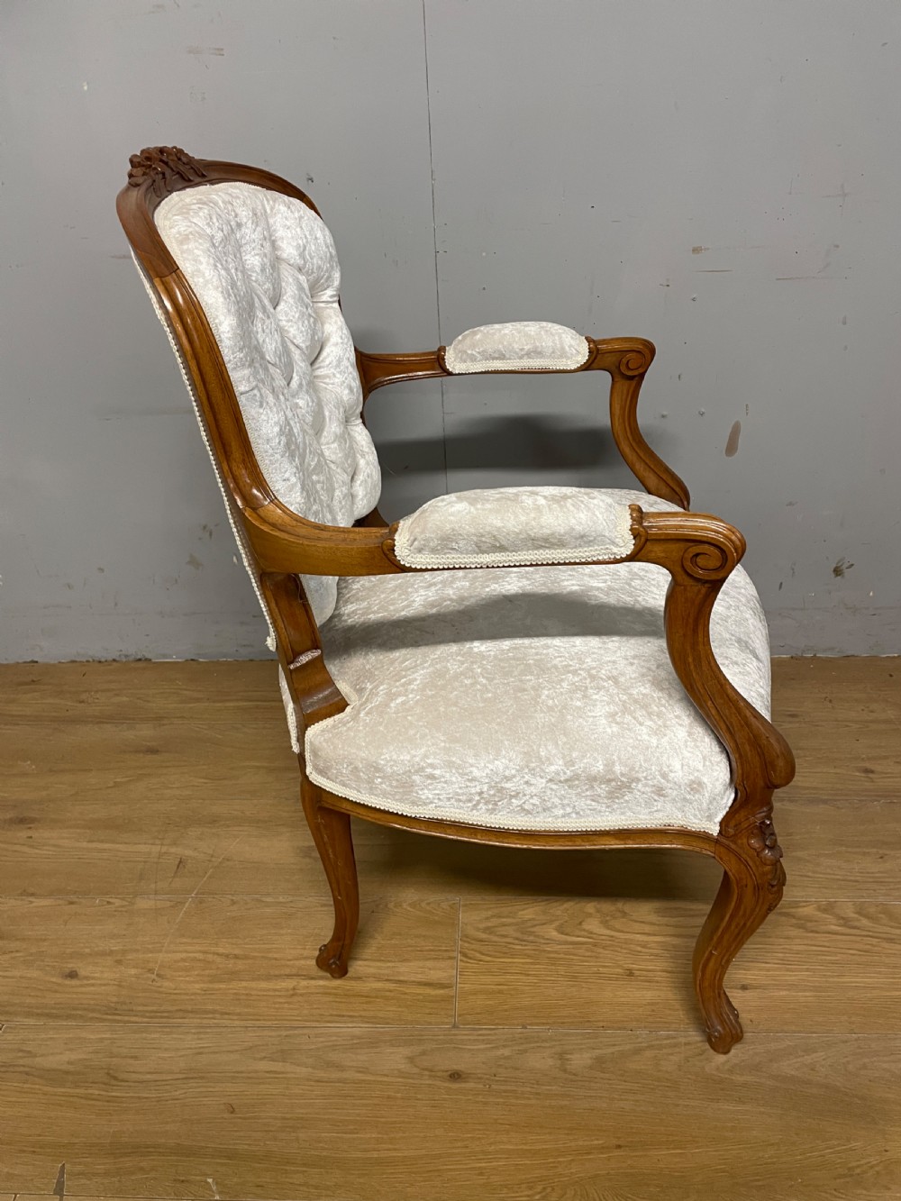 A Louis XV style solid walnut armchair featuring button-tufted cream velvet upholstery, carved cresting, and cabriole legs. View V