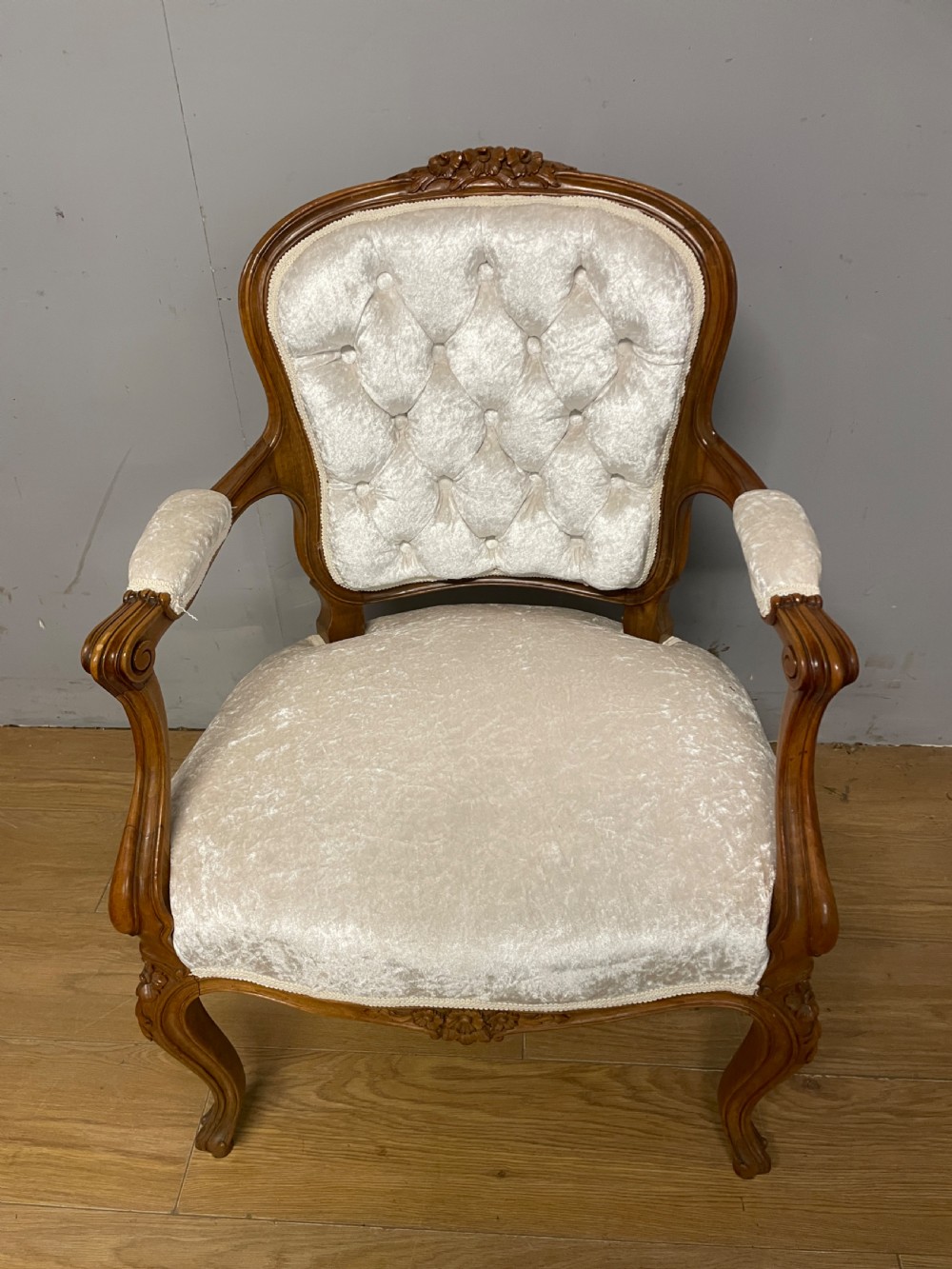 A carved walnut armchair featuring a deep button-tufted cream velvet backrest, padded armrests, and curved cabriole legs.