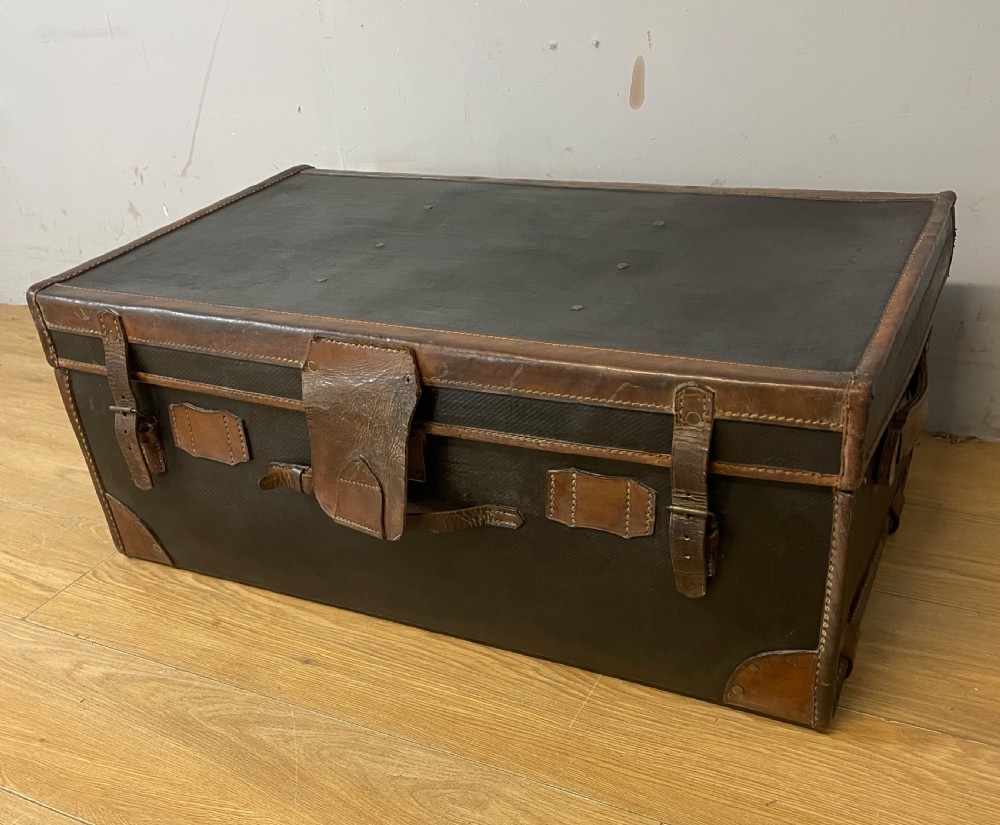 A late 19th-century rectangular black canvas travel trunk featuring brown leather trim, corner protectors, and buckle straps.