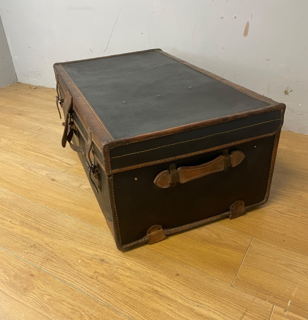 A late 19th-century rectangular black canvas travel trunk featuring brown leather trim, corner protectors, and buckle straps. View II