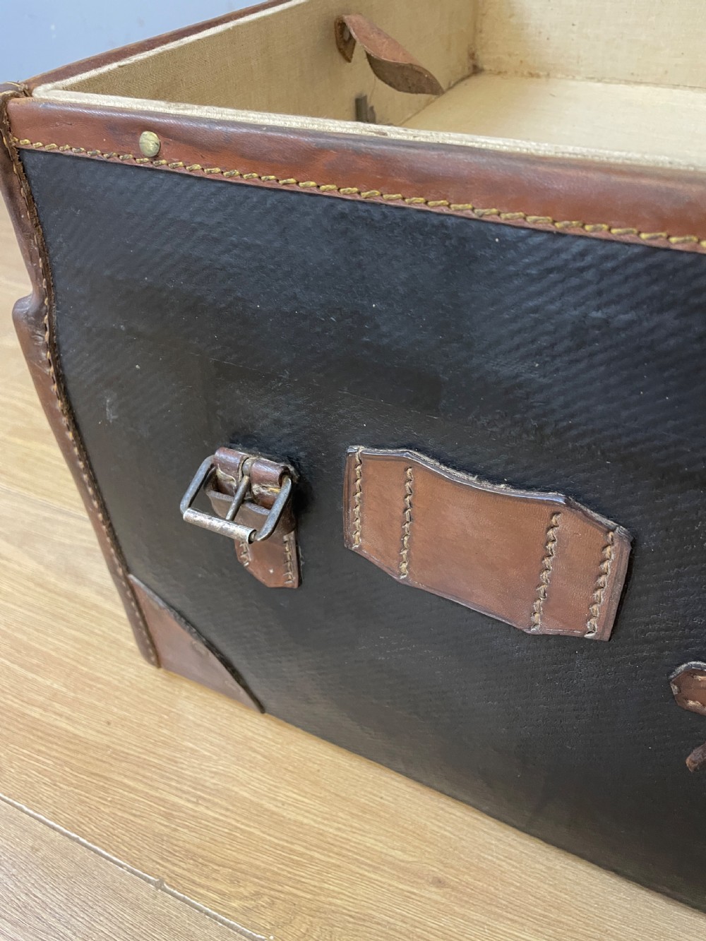 A late 19th-century rectangular black canvas travel trunk featuring brown leather trim, corner protectors, and buckle straps. View VI