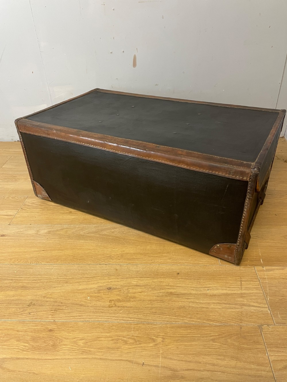 A late 19th-century rectangular black canvas travel trunk featuring brown leather trim, corner protectors, and buckle straps. View X