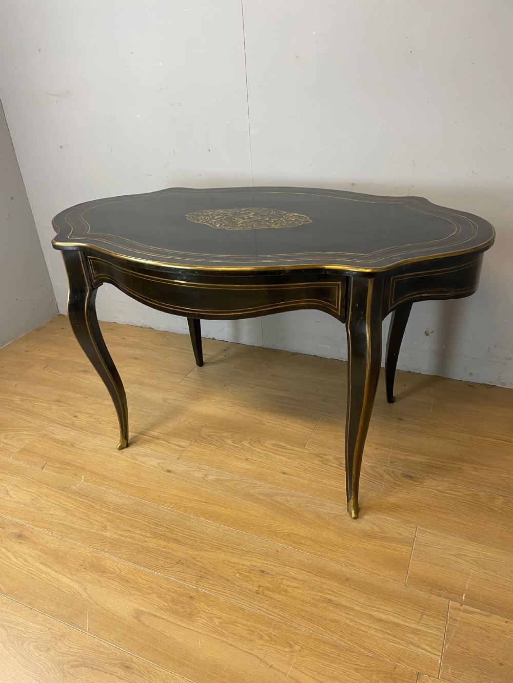 A 19th-century French ebonised writing table featuring brass inlay, a serpentine shaped top, and cabriole legs.
