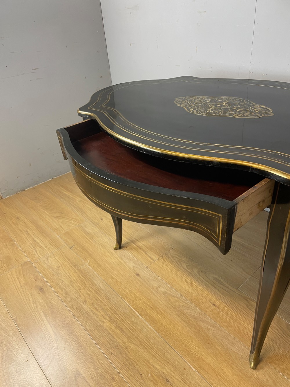 A 19th-century French ebonised writing table featuring brass inlay, a serpentine shaped top, and cabriole legs. View VI
