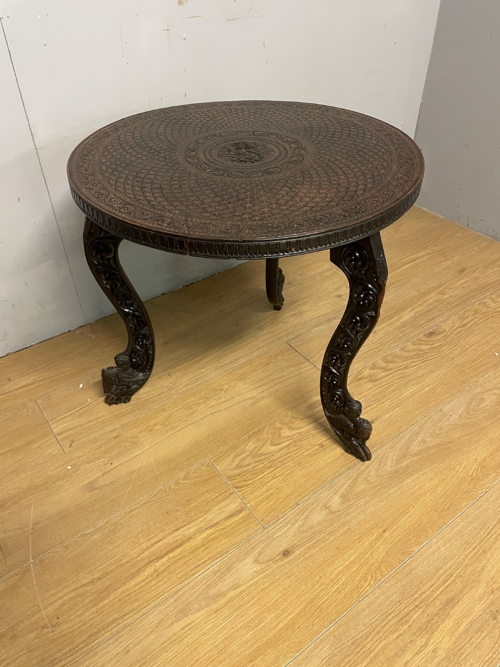 A circular 19th-century Anglo-Indian dark wood side table with intricate hand-carved floral patterns on the tabletop and cabriole legs.