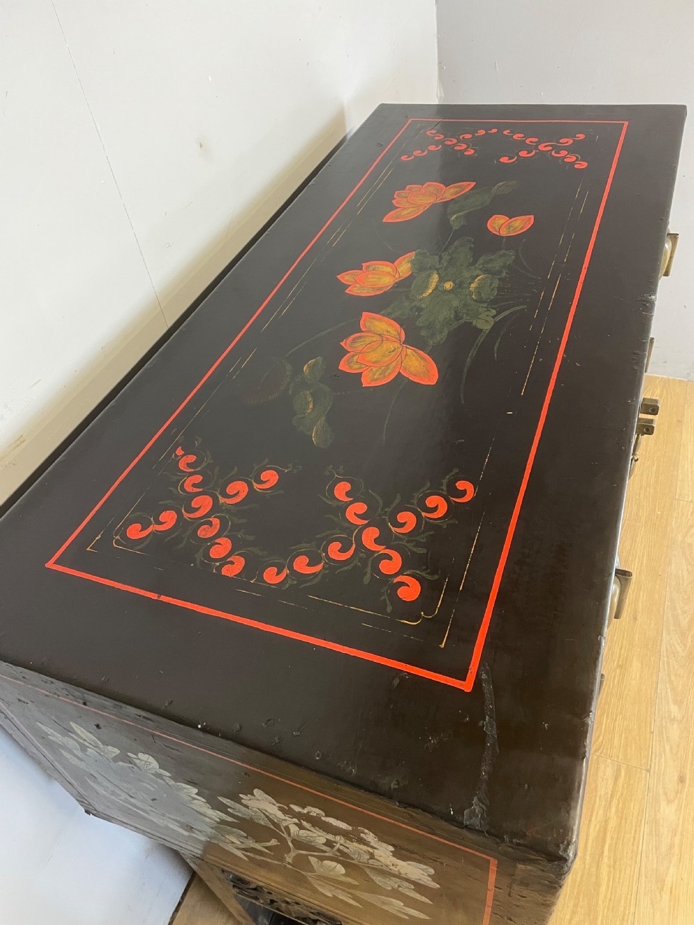 An antique black lacquered cabinet featuring hand-painted landscape scenes and large rectangular brass hinges, elevated on a dark wooden open stand. View V