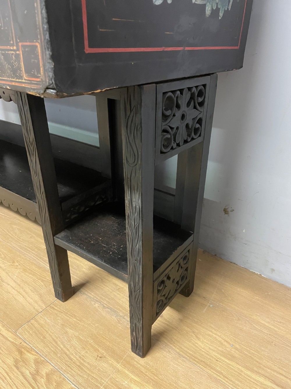 An antique black lacquered cabinet featuring hand-painted landscape scenes and large rectangular brass hinges, elevated on a dark wooden open stand. View VIII