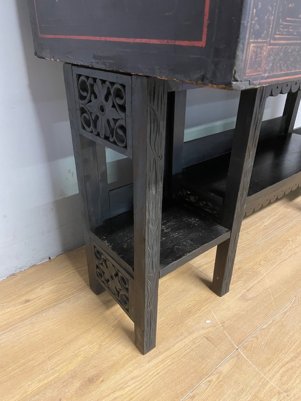 An antique black lacquered cabinet featuring hand-painted landscape scenes and large rectangular brass hinges, elevated on a dark wooden open stand. View IX