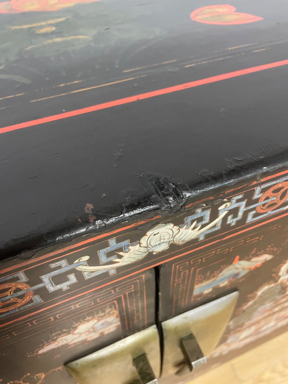 An antique black lacquered cabinet featuring hand-painted landscape scenes and large rectangular brass hinges, elevated on a dark wooden open stand. View XI