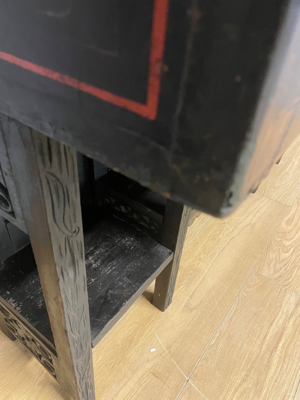 An antique black lacquered cabinet featuring hand-painted landscape scenes and large rectangular brass hinges, elevated on a dark wooden open stand. View XII