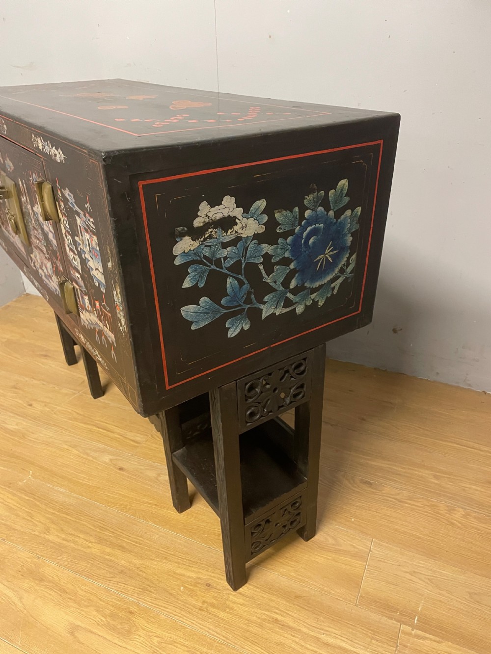 An antique black lacquered cabinet featuring hand-painted landscape scenes and large rectangular brass hinges, elevated on a dark wooden open stand. View XIII