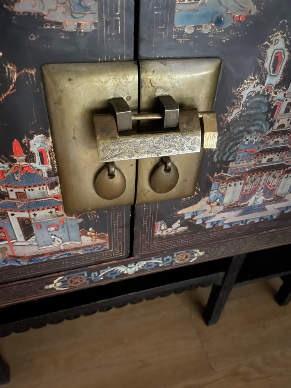 An antique black lacquered cabinet featuring hand-painted landscape scenes and large rectangular brass hinges, elevated on a dark wooden open stand. View XIV