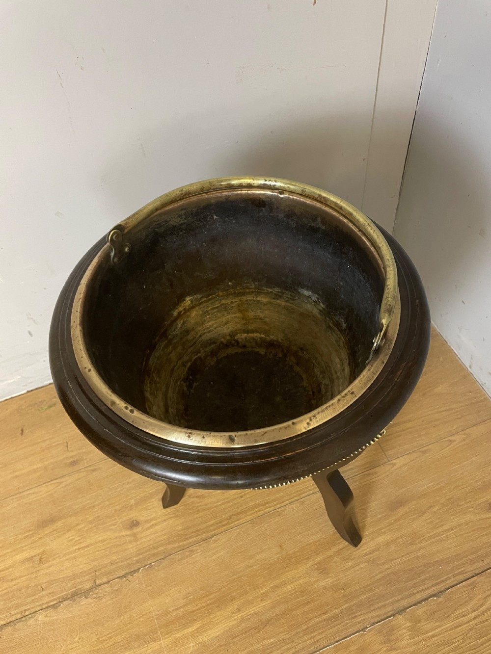 An Edwardian wine cooler featuring a removable brass bucket with a swing handle, supported within a slatted mahogany tripod stand adorned with brass lion mask mounts and decorative chains. View VI