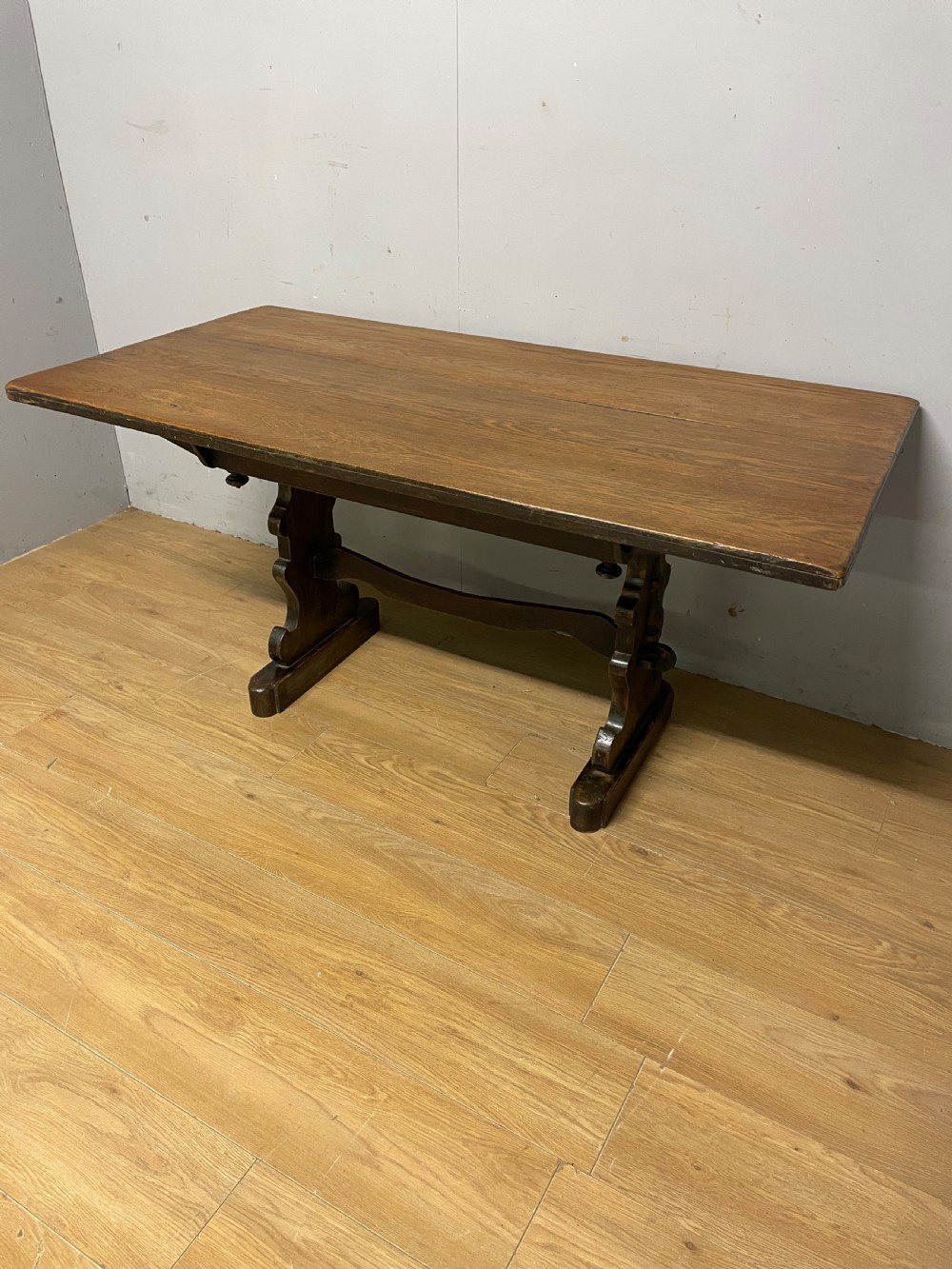 An Arts and Crafts oak refectory dining table featuring a rectangular top supported by shaped trestle end supports connected by a stretcher.