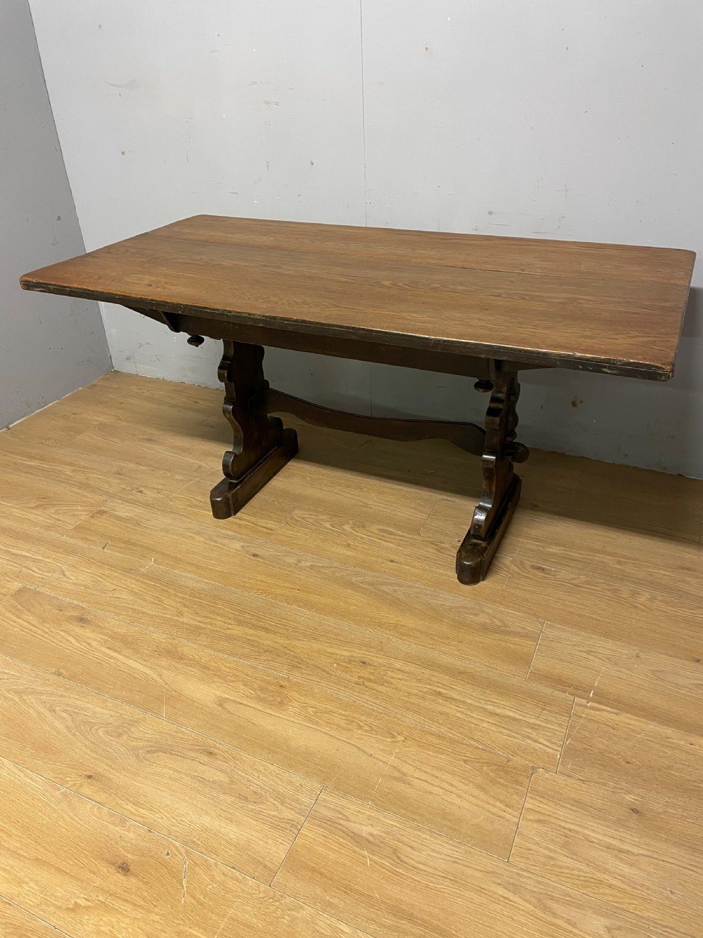 An Arts and Crafts oak refectory dining table featuring a rectangular top supported by shaped trestle end supports connected by a stretcher. View II