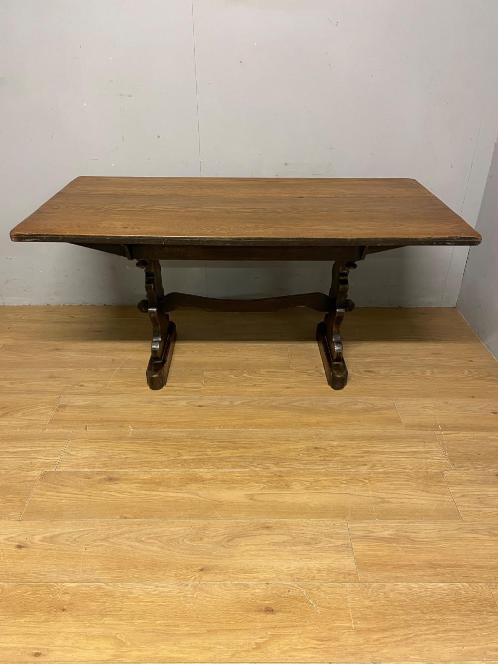 An Arts and Crafts oak refectory dining table featuring a rectangular top supported by shaped trestle end supports connected by a stretcher. View III