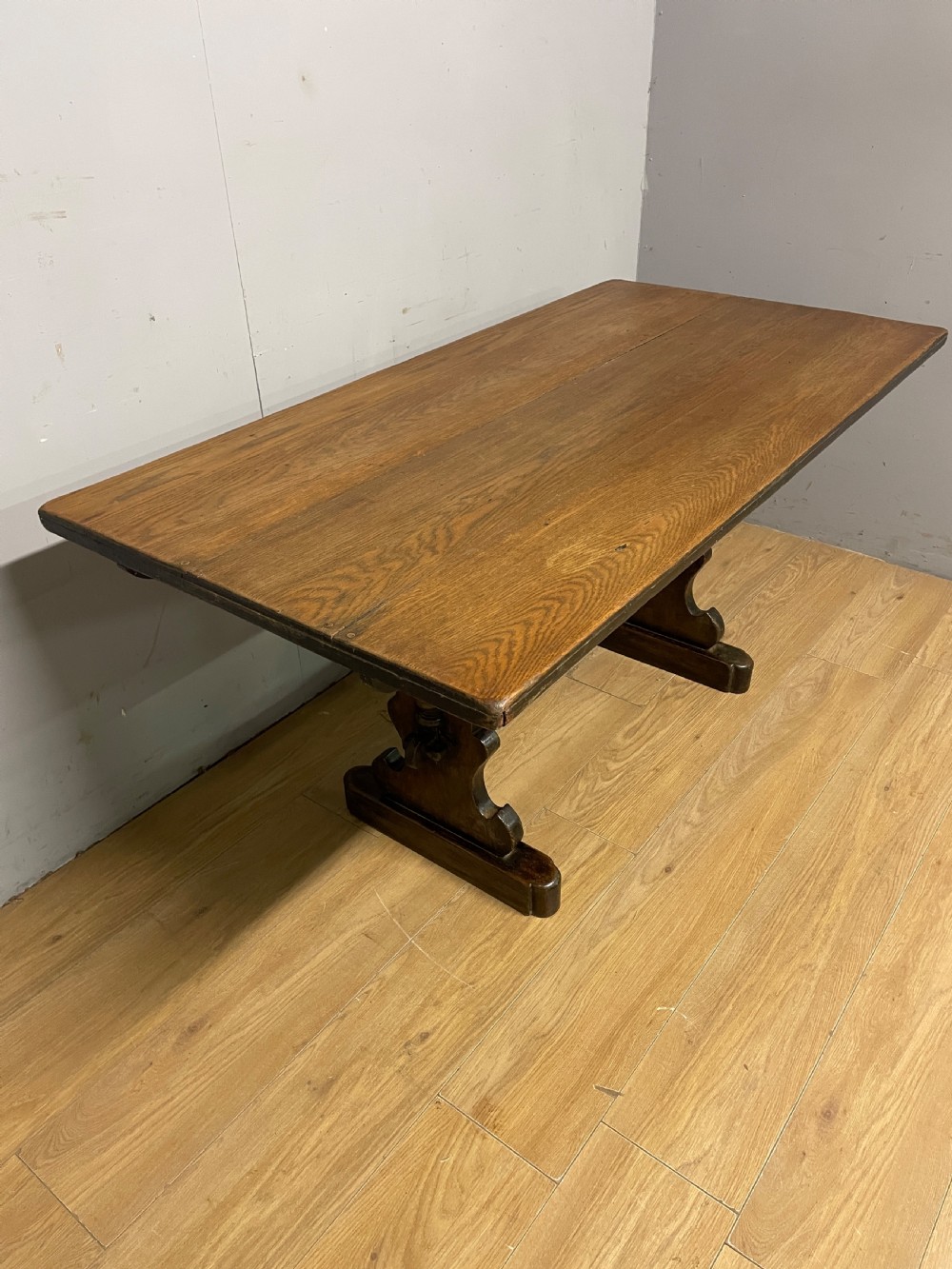 An Arts and Crafts oak refectory dining table featuring a rectangular top supported by shaped trestle end supports connected by a stretcher. View IV
