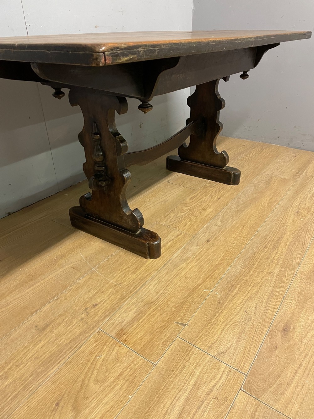 An Arts and Crafts oak refectory dining table featuring a rectangular top supported by shaped trestle end supports connected by a stretcher. View V