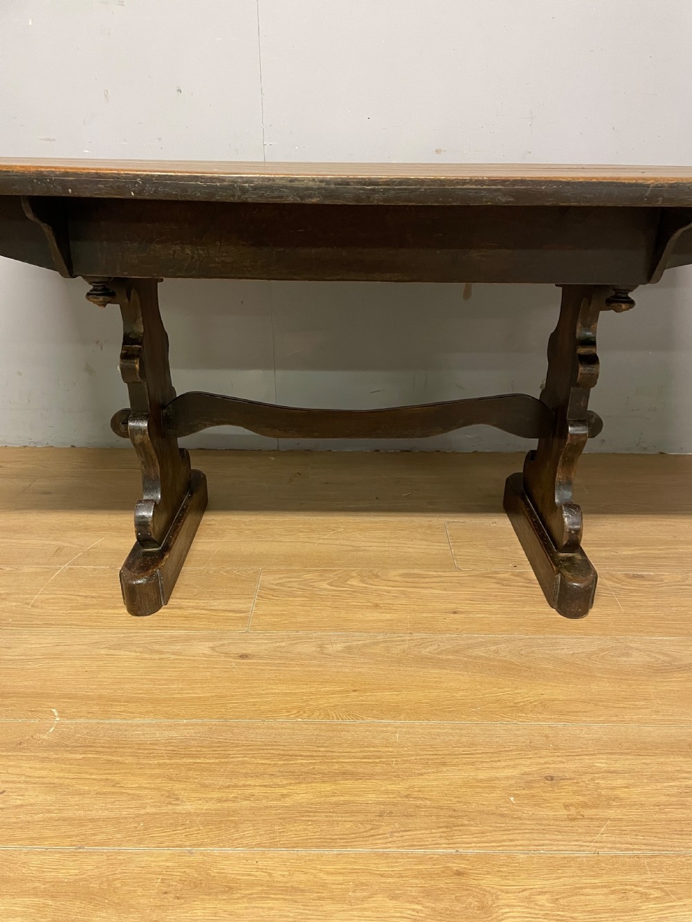 An Arts and Crafts oak refectory dining table featuring a rectangular top supported by shaped trestle end supports connected by a stretcher. View VI