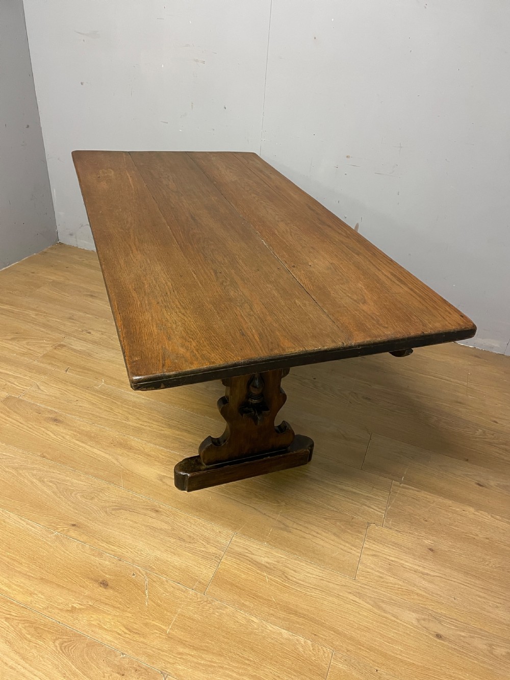 An Arts and Crafts oak refectory dining table featuring a rectangular top supported by shaped trestle end supports connected by a stretcher. View VII