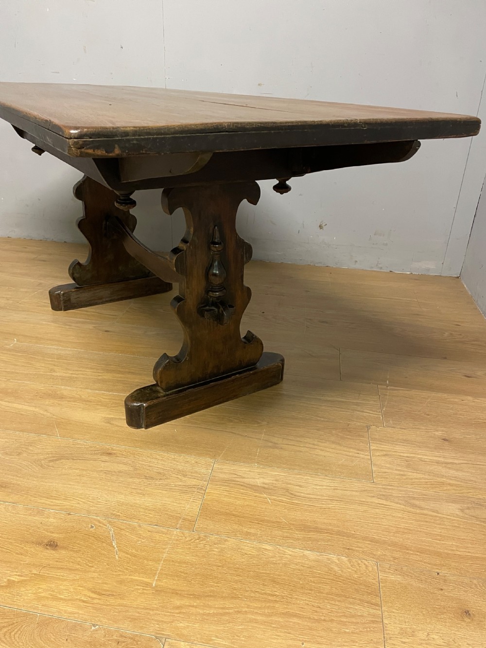 An Arts and Crafts oak refectory dining table featuring a rectangular top supported by shaped trestle end supports connected by a stretcher. View VIII