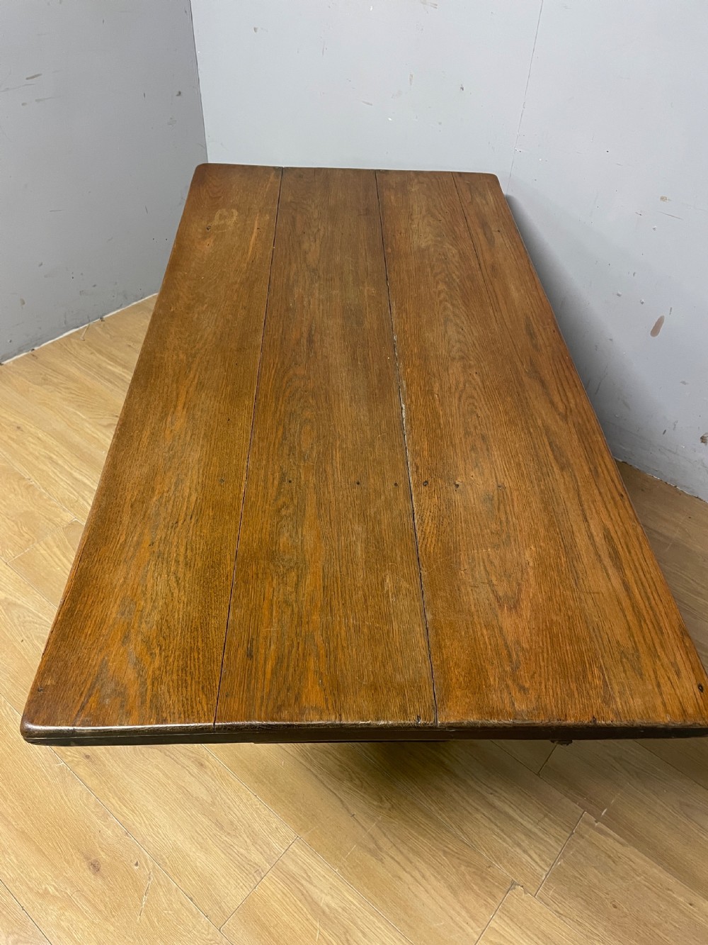 An Arts and Crafts oak refectory dining table featuring a rectangular top supported by shaped trestle end supports connected by a stretcher. View IX