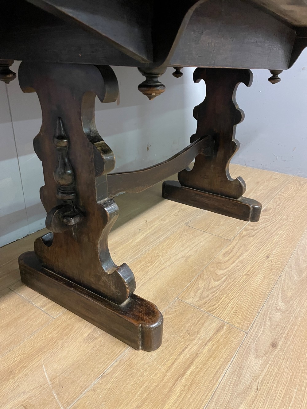 An Arts and Crafts oak refectory dining table featuring a rectangular top supported by shaped trestle end supports connected by a stretcher. View XII