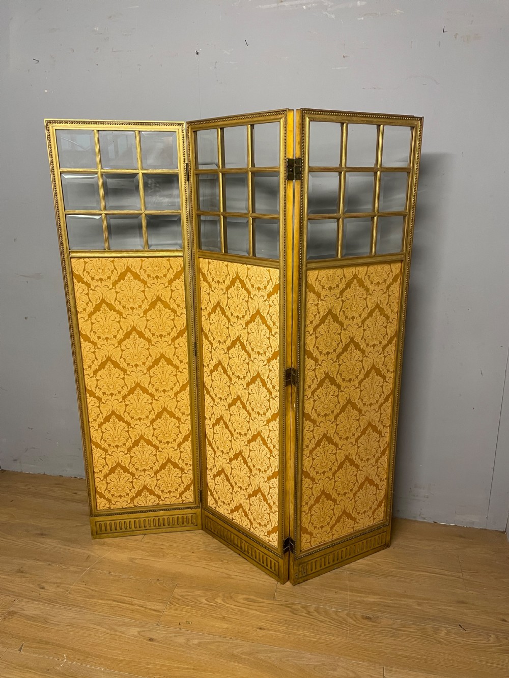 A nineteenth-century three-panel giltwood folding screen featuring glazed upper window panes and golden damask upholstered lower sections.