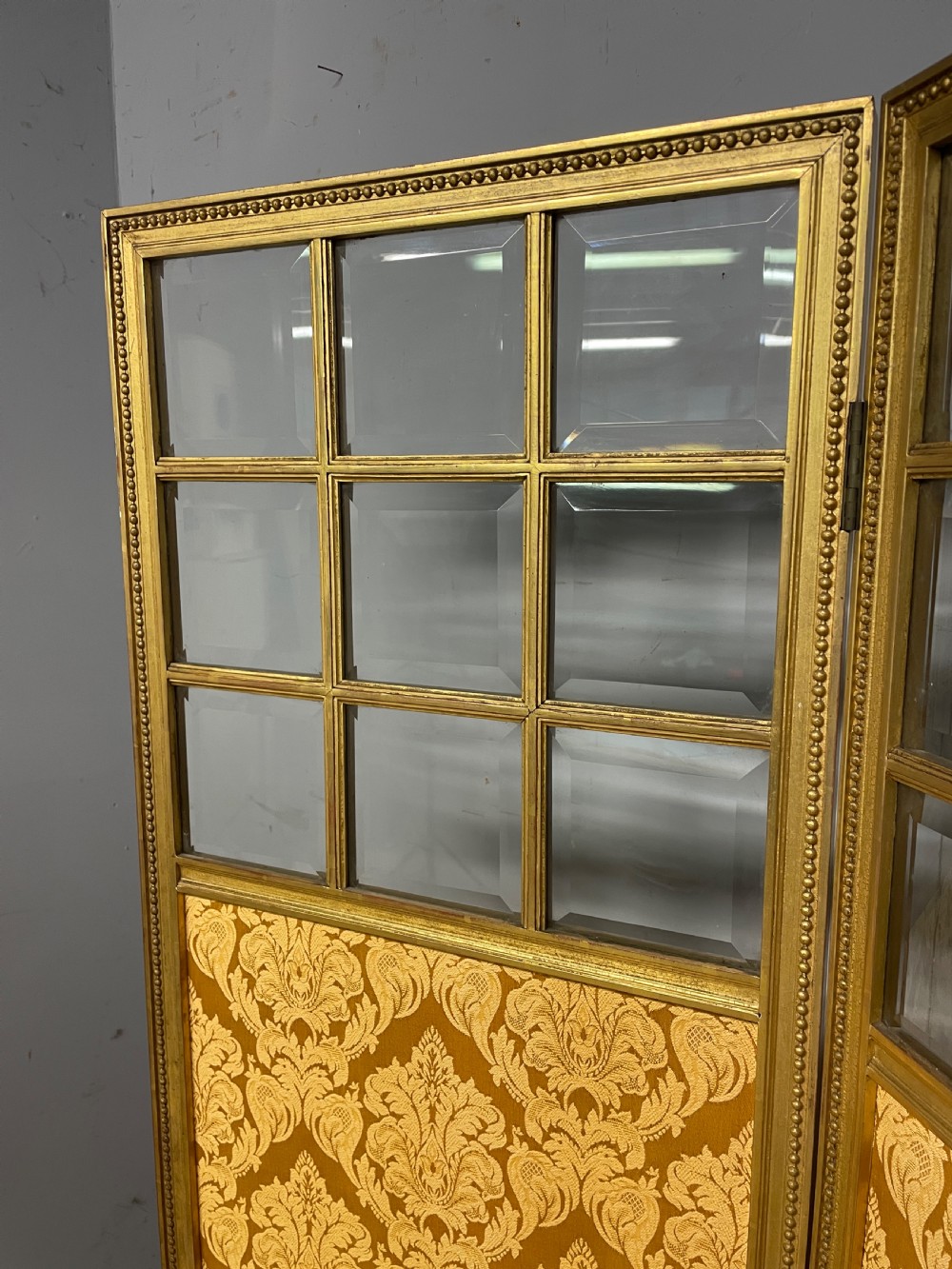 A nineteenth-century three-panel giltwood folding screen featuring glazed upper window panes and golden damask upholstered lower sections. View VI