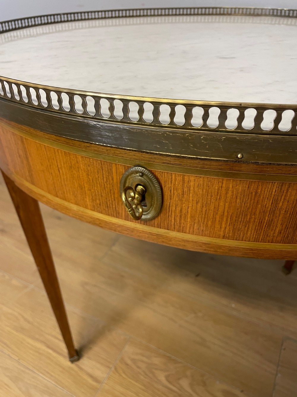 A late 19th-century French circular Bouillotte table featuring a white marble top with a pierced brass gallery, a veneered apron with a small drawer, and four square tapered legs ending in brass sabots. View II